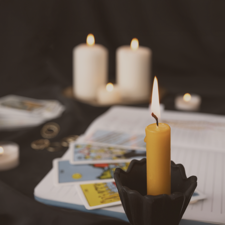 Una candela accesa in primo piano, con degli strumenti di divinazione in secondo piano
