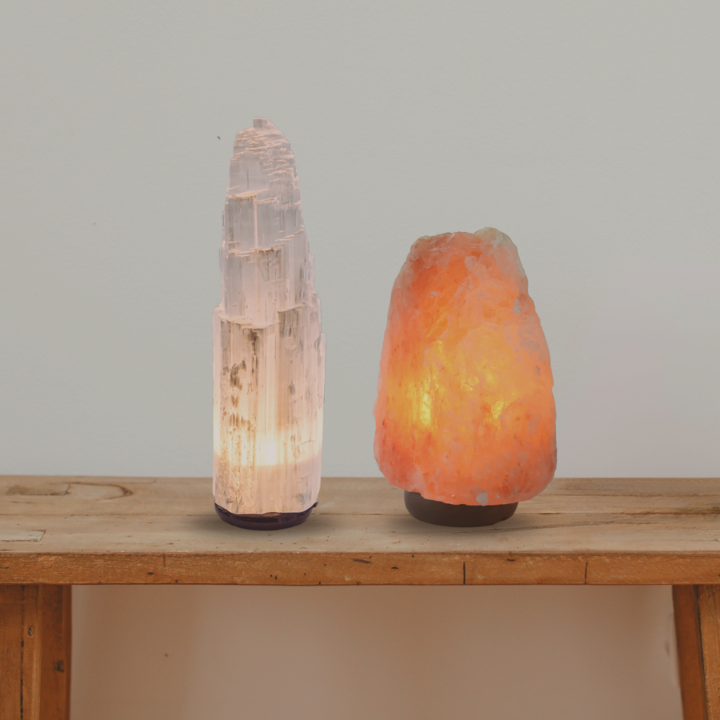 Una lampada di sale e una di selenite entrambe accese, appoggiate su un tavolino di legno
