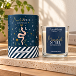Candela profumata Celestial Magic Ambra Baltica e Oud, con confezione illustrata, ambientata su una consolle in legno.