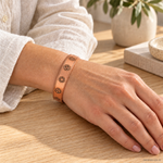 Bracciale magnetico in rame regolabile con simboli dei chakra incisi, indossato al polso.