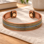 Bracciale magnetico in rame regolabile con quattro file dorate e banda argentata centrale, appoggiato sul lino.