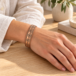 Bracciale magnetico in rame con motivo floreale inciso e bordi puntinati, regolabile e indossato al polso.
