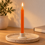 Candela rituale arancio antico tinta nella massa, accesa in un portacandela di ceramica su un vassoio in travertino.