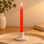 Candela rituale arancione tinta nella massa, accesa in un portacandela di ceramica su un vassoio in travertino.