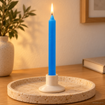 Candela rituale azzurra tinta nella massa, accesa in un portacandela di ceramica su un vassoio in travertino.