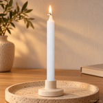 Candela rituale bianca tinta nella massa, accesa in un portacandela di ceramica su un vassoio in travertino.