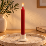 Candela rituale bordeaux tinta nella massa, accesa in un portacandela di ceramica su un vassoio in travertino.