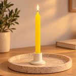 Candela rituale gialla tinta nella massa, accesa in un portacandela di ceramica su un vassoio in travertino.