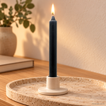 Candela rituale grigia tinta nella massa, accesa in un portacandela di ceramica su un vassoio in travertino.