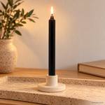 Candela rituale marrone tinta nella massa, accesa in un portacandela di ceramica su un vassoio in travertino.