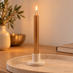 Candela rituale oro tinta nella massa, accesa in un portacandela di ceramica su un vassoio in travertino.