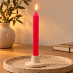 Candela rituale rosa fucsia tinta nella massa, accesa in un portacandela di ceramica su un vassoio in travertino.