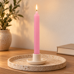 Candela rituale rosa tinta nella massa, accesa in un portacandela di ceramica su un vassoio in travertino.