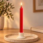 Candela rituale rossa tinta nella massa, accesa in un portacandela di ceramica su un vassoio in travertino.