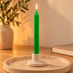 Candela rituale verde tinta nella massa, accesa in un portacandela di ceramica su un vassoio in travertino.