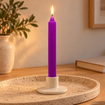 Candela rituale viola tinta nella massa, accesa in un portacandela di ceramica su un vassoio in travertino.