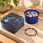Candela Capricorno dello Zodiaco con confezione e braccialetto, ambientata su una consolle in legno.